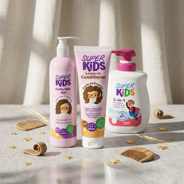 Three Super Kids hair care products arranged on a light stone surface with decorative combs and gold star confetti. The set includes a pink pump bottle of curly hair gel, a white squeeze tube of leave-in conditioner, and a white pump bottle of 3-in-1 shampoo, all with colorful cartoon labels.